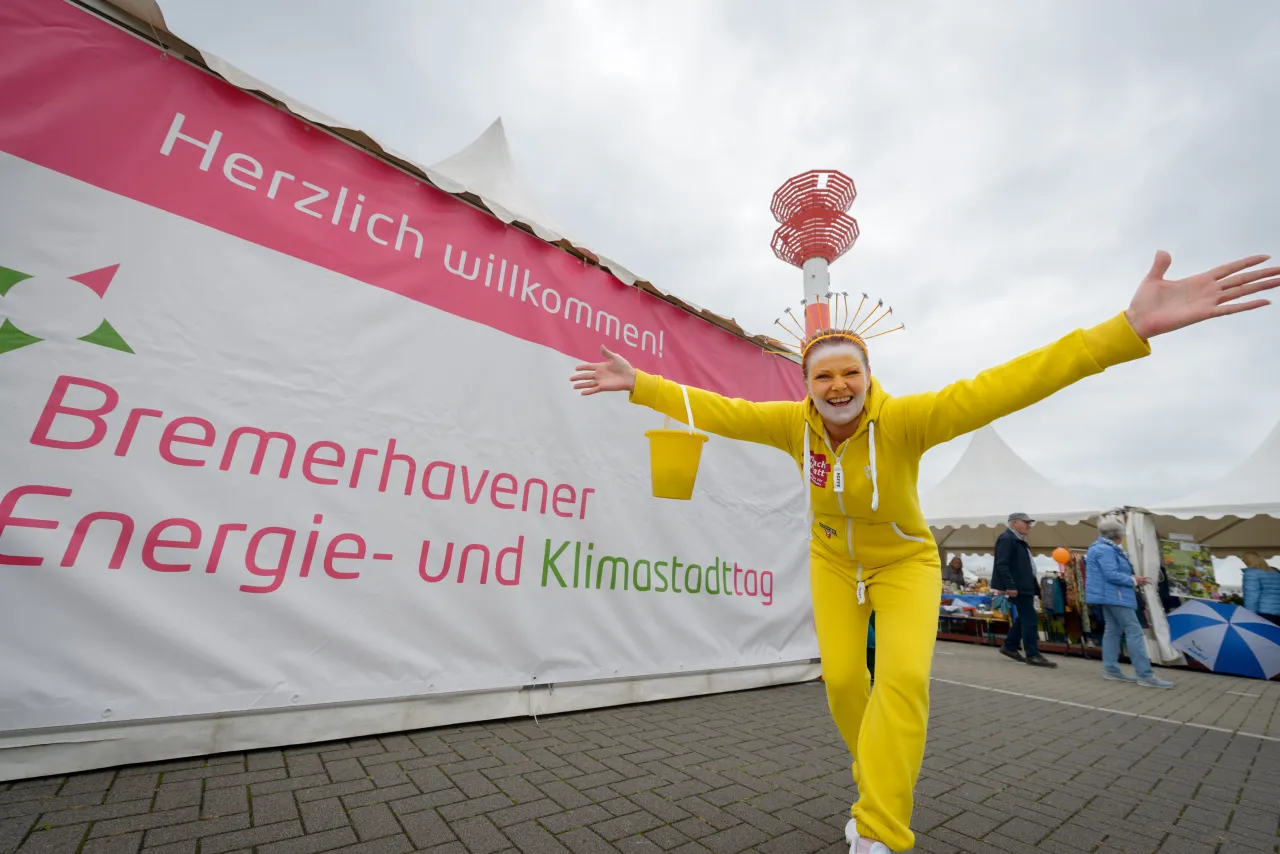Person im Sonnen Kostum steht vor einem Banner mit der Aufschrift 